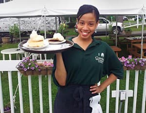 A smiling Gavin's server carrying a tray at an outdoor summer event