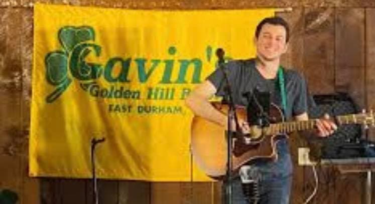 Sean Feeney playing guitar in front of the Gavin's Golden Hill Pub banner